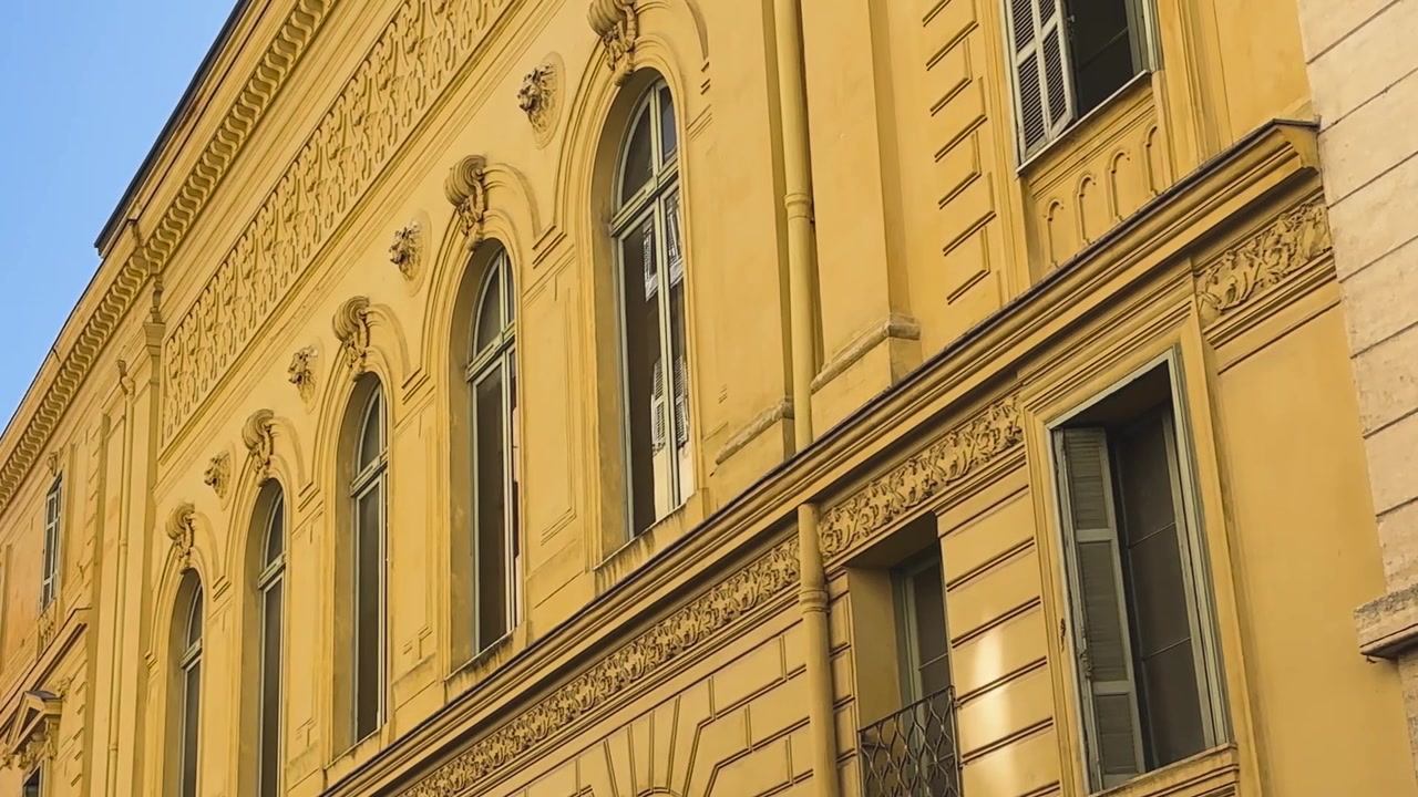 Elegante facciata storica gialla con alte finestre ad arco e dettagli architettonici decorativi a Nizza, Francia, sulla Costa Azzurra
