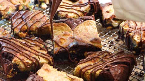 baking chocolate brownies with added confetti sugar cookies, called a brookie. close up and panning across brownies drizzled with melted chocolate on a wire rack. in the kitchen making a dessert
