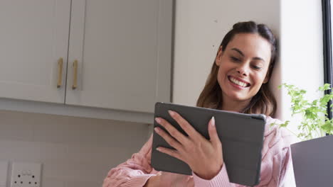 at home, woman in pink sweater smiling while using tablet near window, copy space