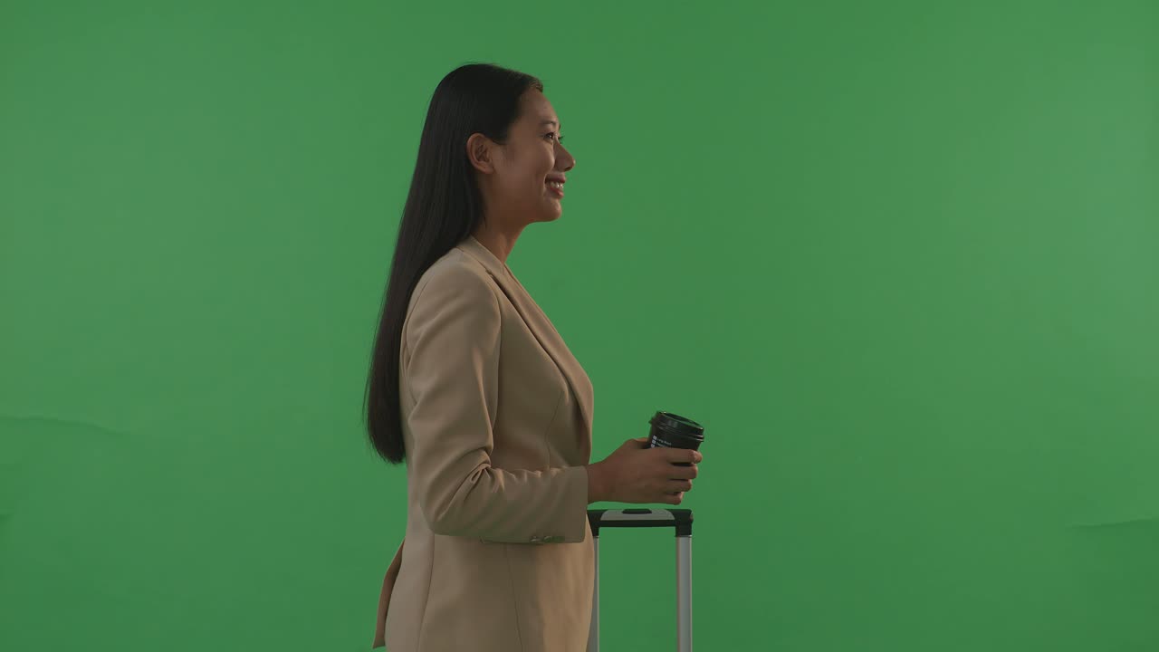 Side View Asian Businesswoman Traveler With Luggage Drinking Coffee While Standing In The Green Screen Background Studio, During Sunset Time