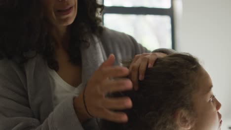 Happy-mixed-race-mother-and-daughter-brushing-hair-in-bedroom