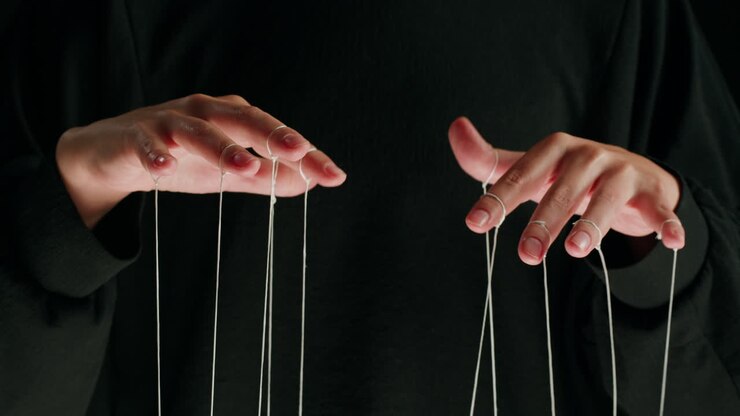 Hands of a Puppeteer Manipulating Strings on a Dark Background