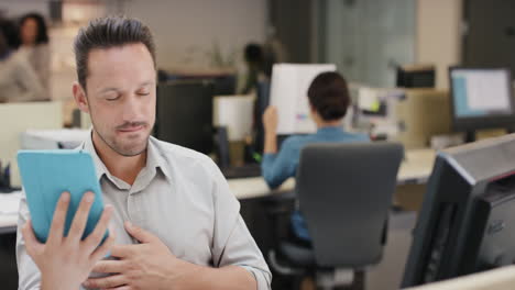 Businessman-executive-working-at-computer-using-digital-tablet-connected-to-global-data-in-busy-corporate-office-committed-to-growth-and-success