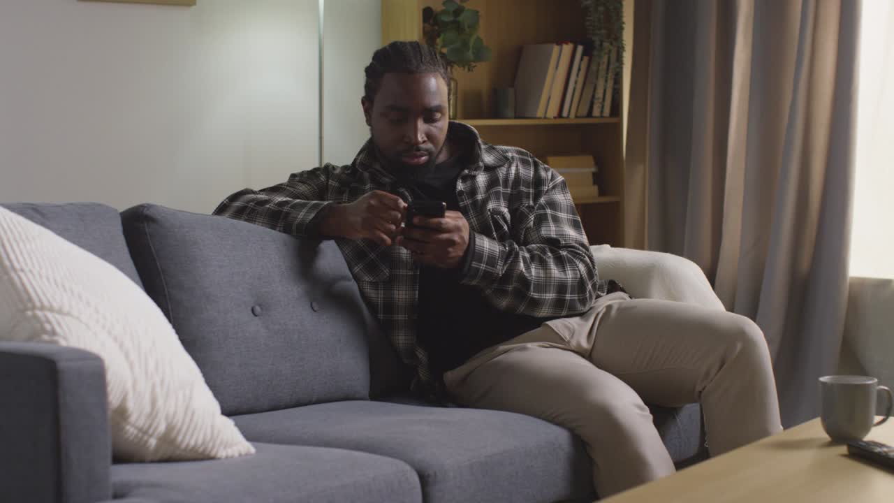 hombre relajándose en casa sentado en el sofá desplazándose por el teléfono móvil