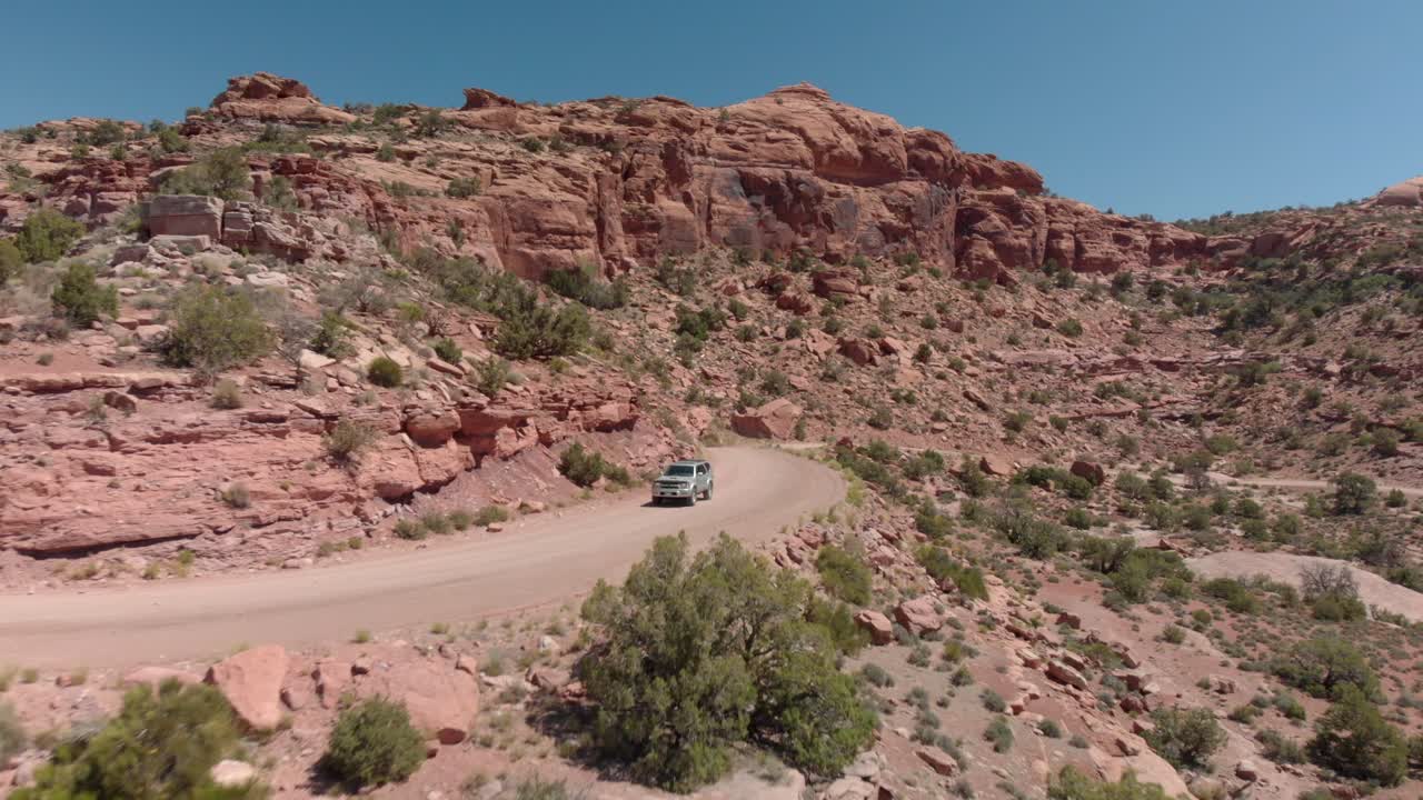 Ripresa aerea segue un SUV argentato attorno a una curva su una strada sterrata in un paesaggio canyonico