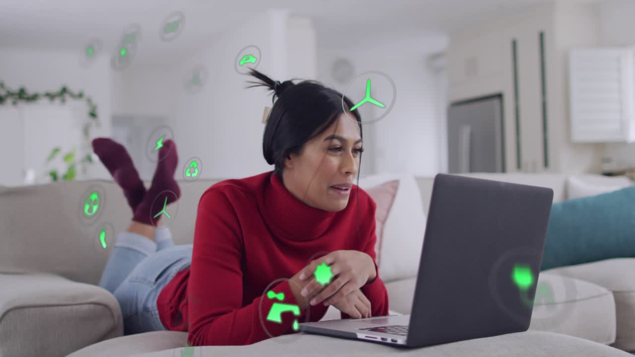 Woman lying on sofa using laptop, tapping screen, researching energy icons covering hands