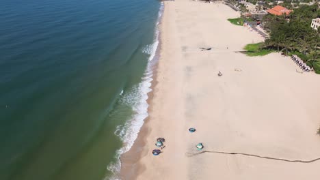 drone flies forward over mui ne beach, panning up from a top-down view to reveal the shoreline, sea on the left, and beachfront resorts on the right.