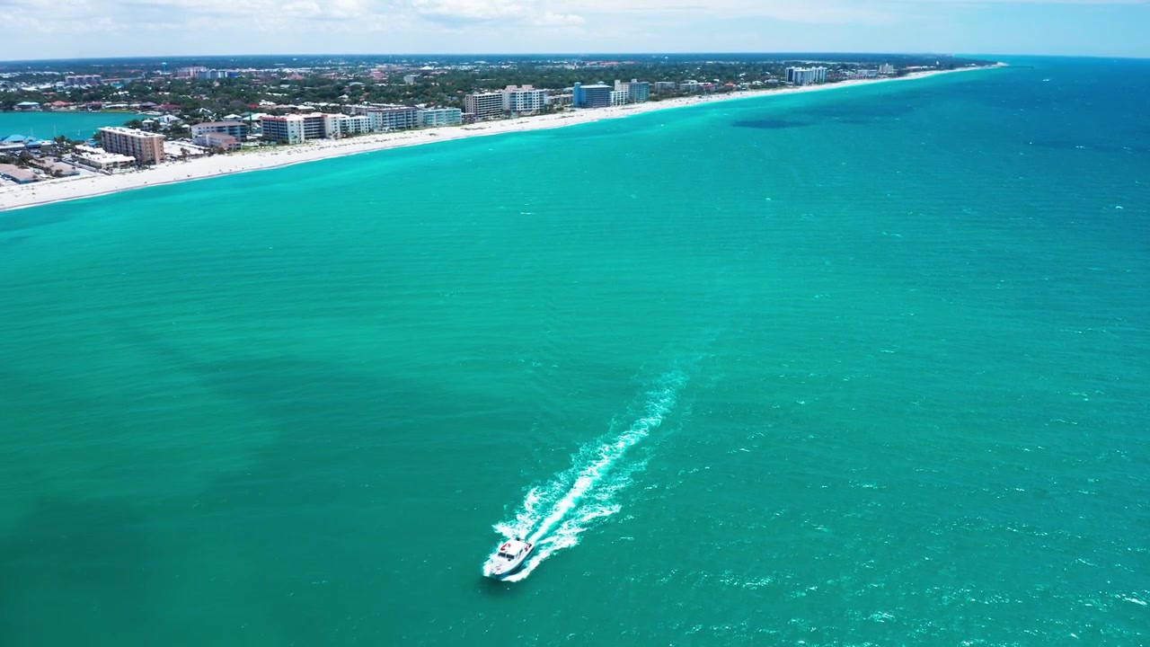 Un motoscafo crea una scia bianca attraverso acque color acquamarina vicino a una fila di edifici costieri. Cattura il movimento vivace dell'imbarcazione contro il mare calmo. Ideale per contenuti di viaggio.