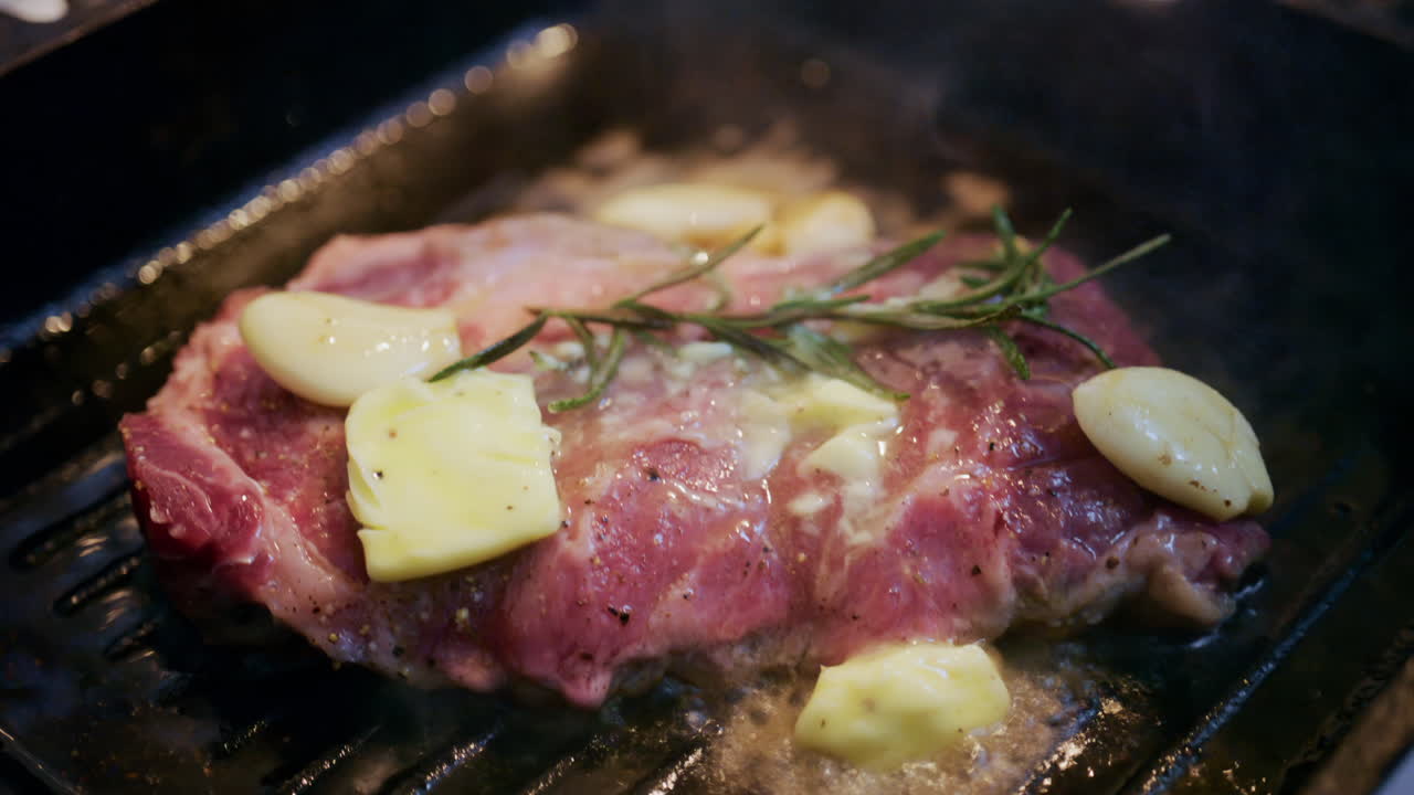 Primer plano de mantequilla derritiéndose sobre un bistec con ajo y romero en una sartén caliente.