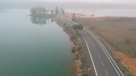 a frontal shot of a white car coming towards the camera in by a road between two lakes