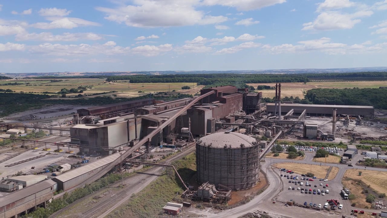 Industrial Steel manufacturing facility featuring large storage tanks and factory buildings set within a expansive landscape under a clear blue sky during the middle of the afternoon