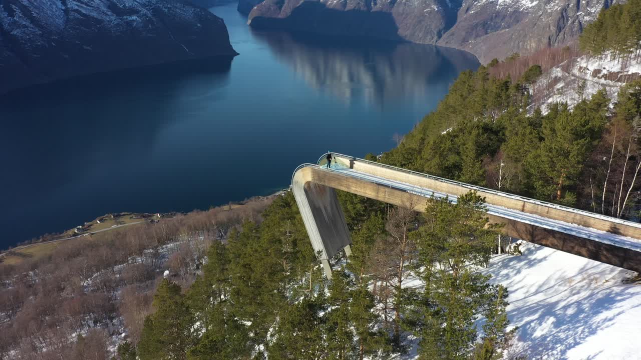 impresionante vista aérea de segastein vista aérea de gran altitud con una persona parada en el borde - girando alrededor del punto de vista para revelar el fiordo y el pueblo de aurland en el fondo muy abajo