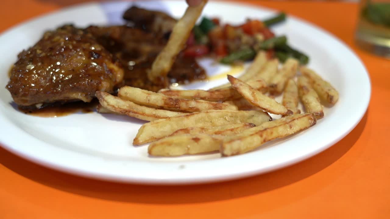 Close up view of roasted chicken served on a white plate in a restaurant along with fried asparagus, carrot, French fries, red pepper and rosemary