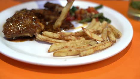 vista de cerca del pollo asado servido en un plato blanco en un restaurante junto con espárragos fritos, zanahoria, papas fritas, pimiento rojo y romero