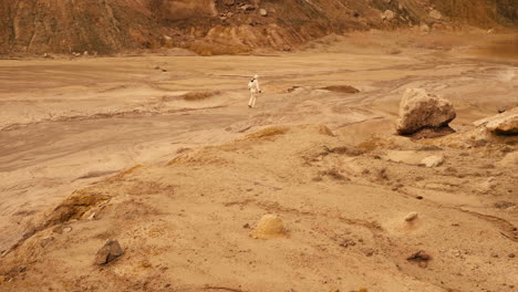 Wide-shot-of-an-astronaut-wearing-a-spacesuit,-moving-across-a-deserted-planet-with-red-soil-and-rocks-looks-off-into-the-distance