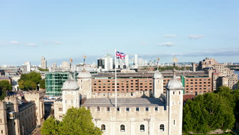 Flying-around-top-of-historic-stone-keep-in-Tower-of-London.-Medieval-square-building-with-four-towers-in-corners.-British-national-flag-on-high-pole.-London,-UK