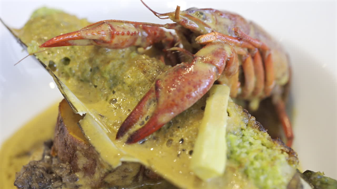 Close up of whole cooked crayfish with a mussel shell filled and a creamy herb topping on a white plate