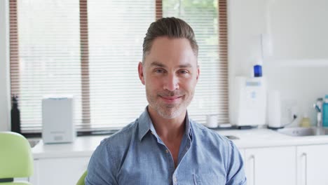 Portrait-of-smiling-caucasian-male-patient-sitting-on-chair-at-modern-dental-clinic