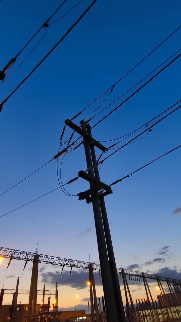 Fotograma de vídeo a ángulo bajo de líneas de alta tensión al atardecer, capturando siluetas industriales contra un crepúsculo
