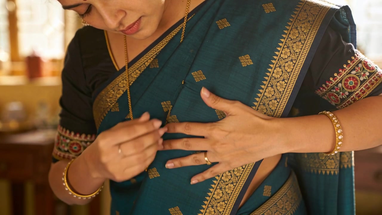 Sintiendo el pallu suelto, mujer india ajustando, pellizcando y alisando un sari color verde azulado en casa, asegurando los pliegues.