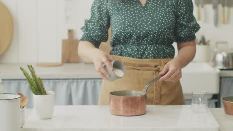 crop woman adding semolina flour in saucepan