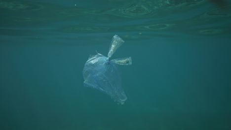 Bolsa-De-Plástico-Flotando-En-Agua-Cristalina-Con-Reflejos-De-Luz-Disparados-Desde-El-Agua.