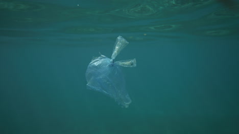 bolsa de plástico flotando en agua cristalina con reflejos de luz disparados desde debajo del agua