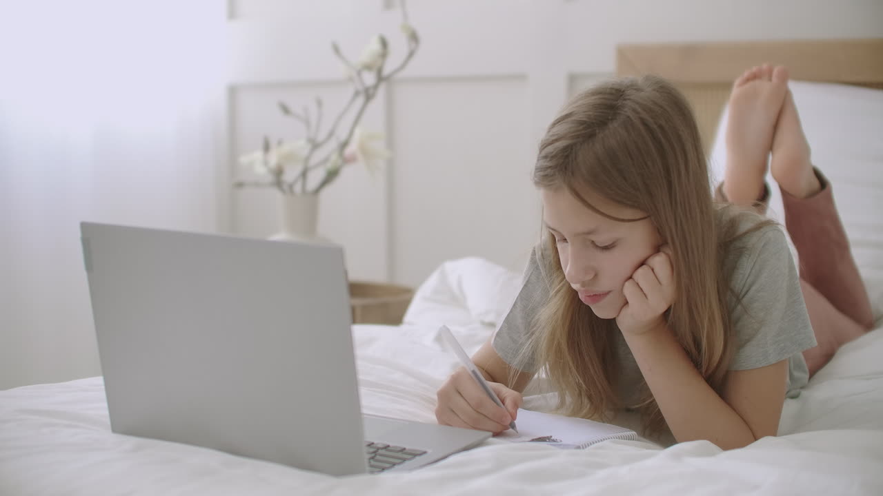 una estudiante aburrida está dibujando en el cuaderno durante la conferencia en línea del maestro en la computadora portátil, la educación en casa y el aprendizaje electrónico de los niños.
