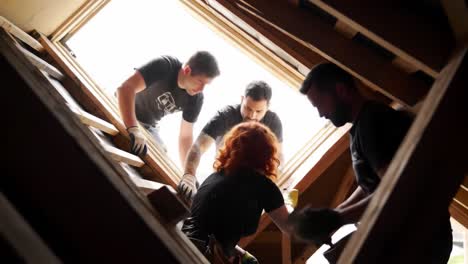 in a bright attic, a construction worker oversees renovations while a colleague handles materials. dust fills the air as they focus on improving the space, showcasing teamwork and craftsmanship.