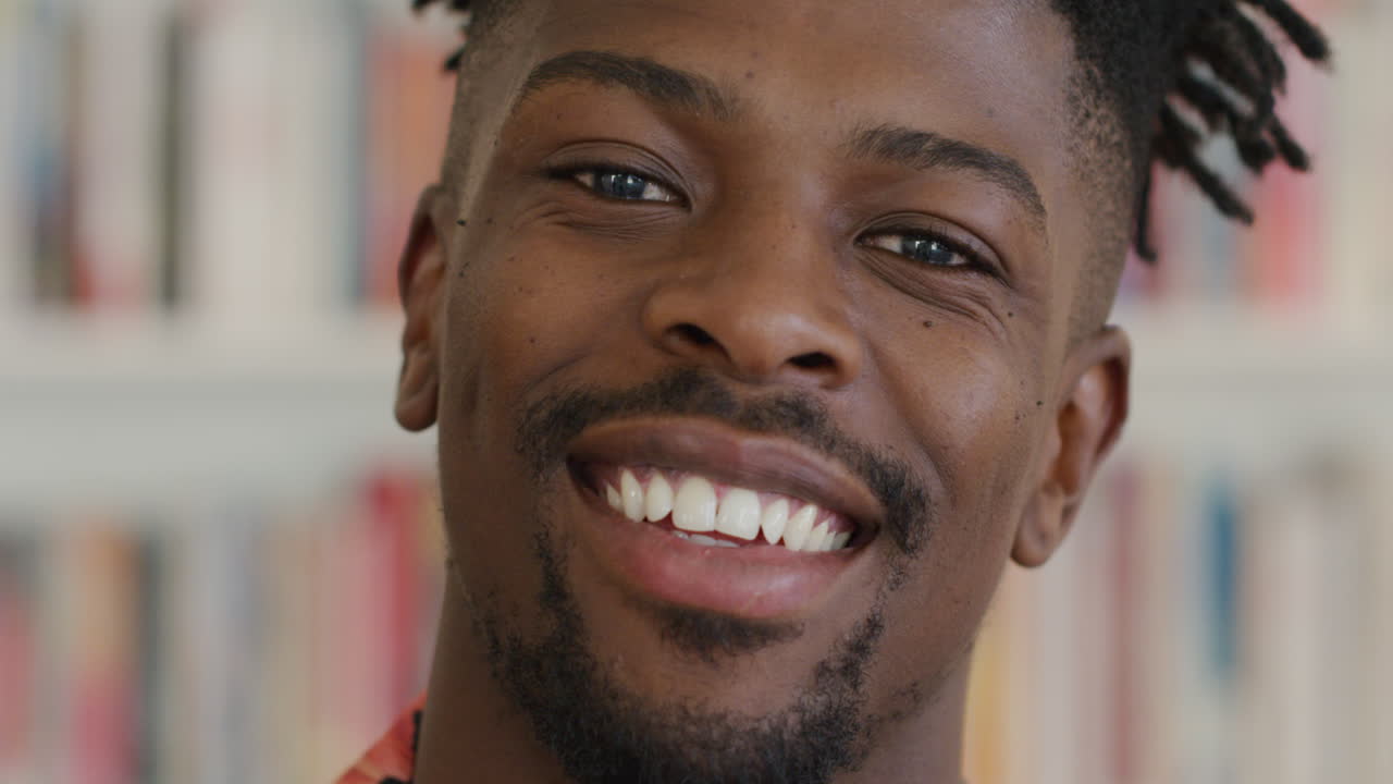 Ritratto di studente afroamericano felice che sorride davanti a uno scaffale di libri in una biblioteca universitaria