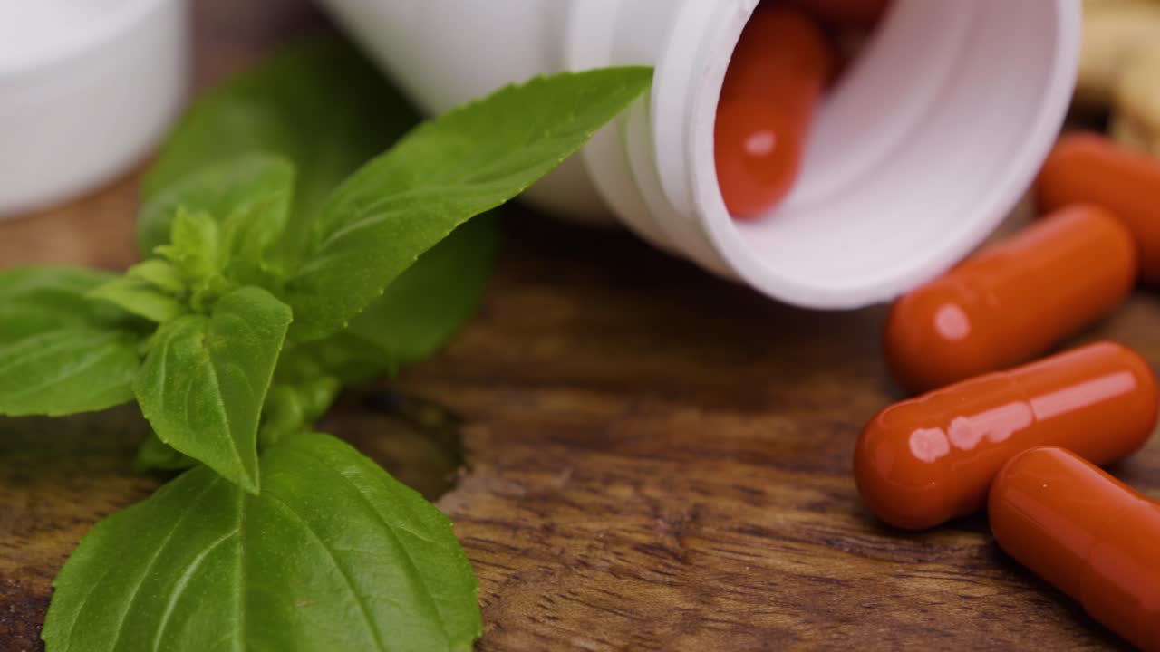 Pan shot from a cutting board with basil, red pills with white tablet wrapper and cashew nuts with cereals
