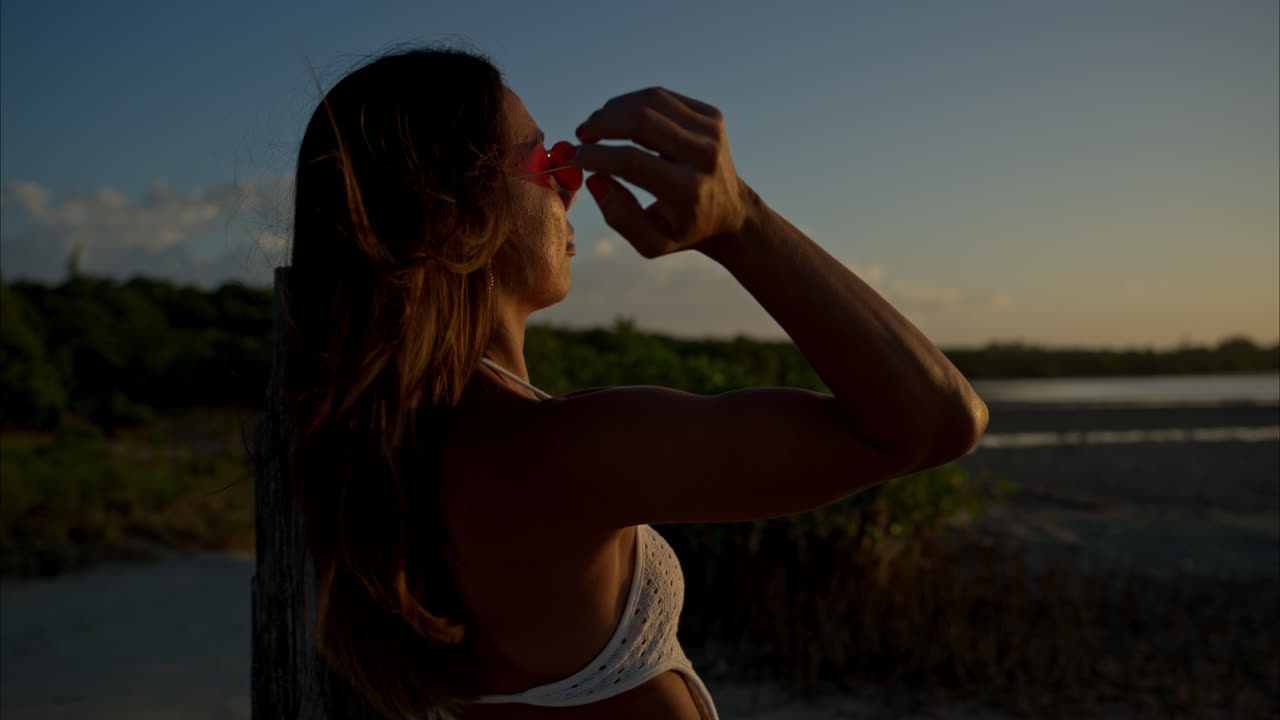 Rallentatore di una donna latina con occhiali da sole che guarda il tramonto e sorride alla telecamera.