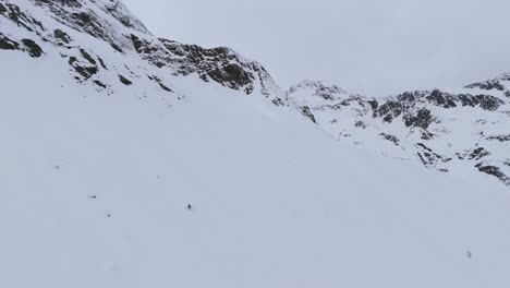 Person-from-far-skiing-down-a-big-snowy-slope-in-alpine-mountains