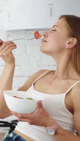 a vegetarian girl sits in the kitchen and eats salad from a plate. healthy diet for weight loss. vertical video
