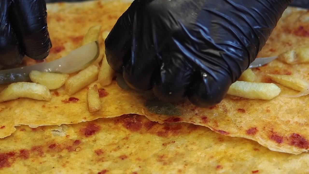 Chef che aggiunge cetriolini a fette a un wrap di pane piatto con patatine fritte