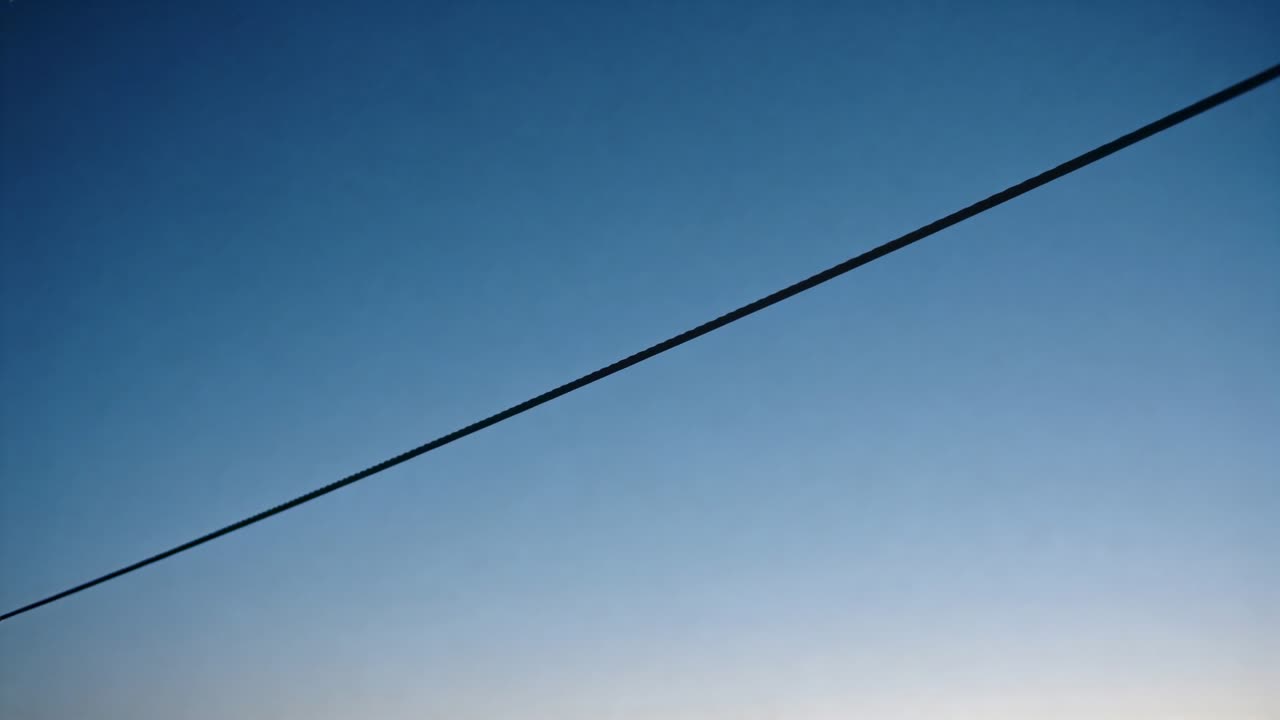 Skiftende diagonalt forsyningskabel glider hen over klar blå himmel under solopgang, horisonten lysner
