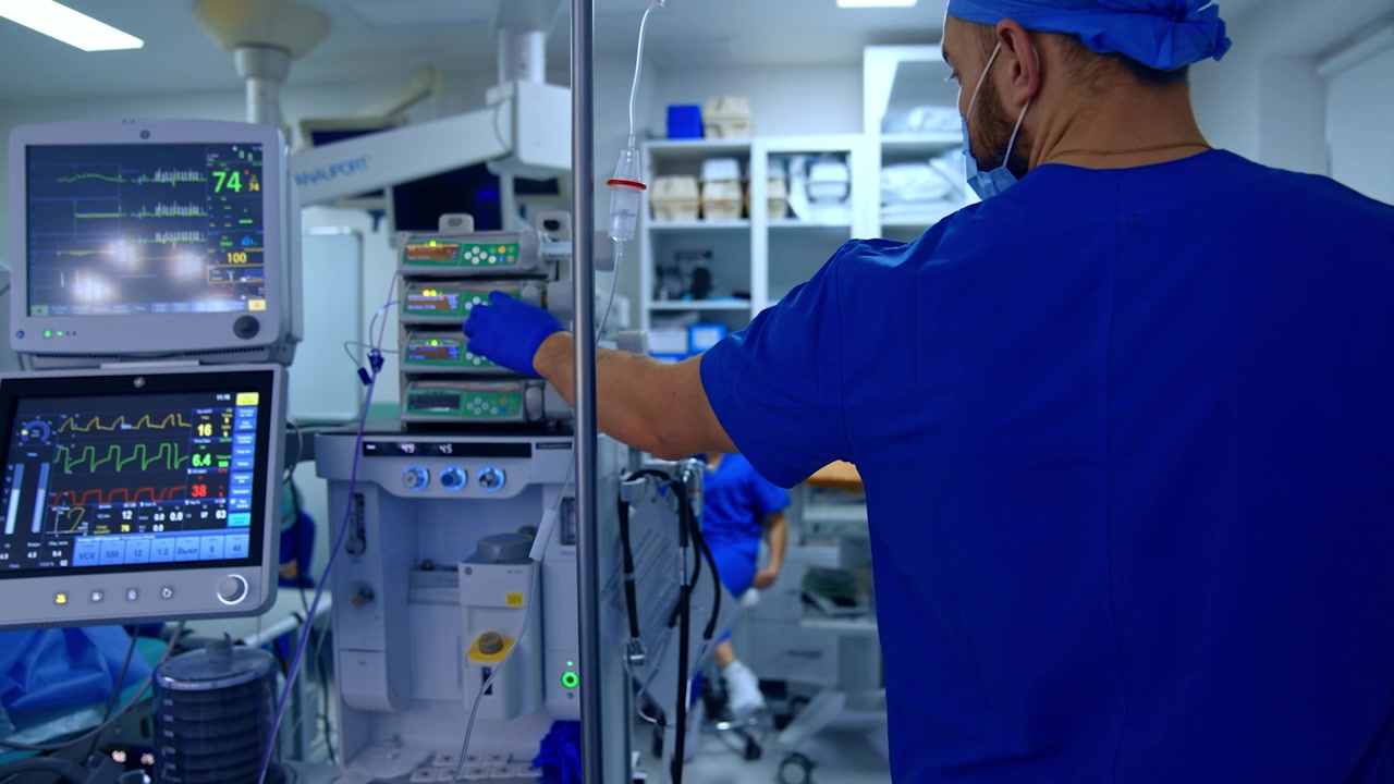 Médico varón con uniforme azul mira los monitores de la máquina de ventilación pulmonar. El doctor presiona un botón en la bomba de infusión médica