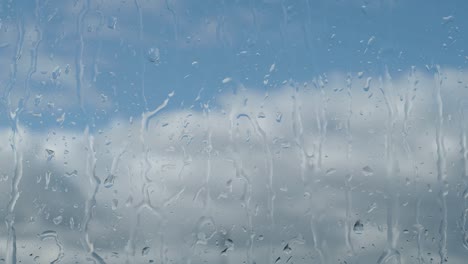 raindrops on a window, blue sky and clouds next to glass of window during rainy day