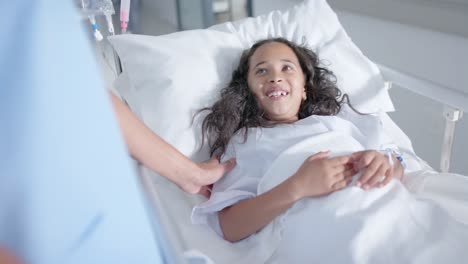 diverse female doctor and child patient talking in corridor at hospital, in slow motion