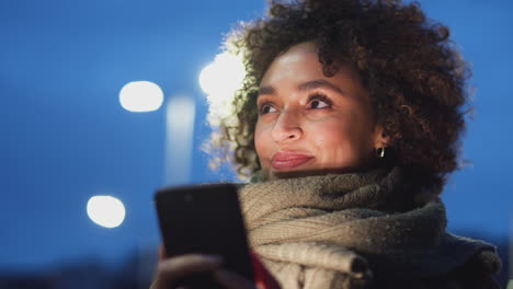 mujer en la calle de la ciudad por la noche ordenando un taxi usando una aplicación de teléfono móvil