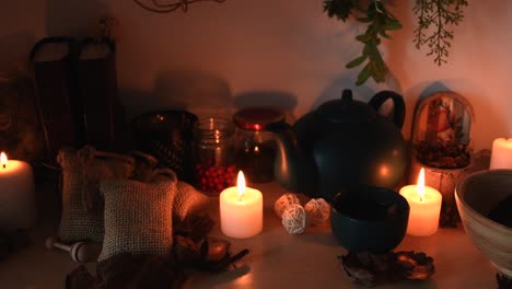 Relaxing-background-detail-shot-of-an-herbal-tea-shop,-with-candles-with-flickering-flames,-a-tea-pot,-a-cup-with-steam-coming-out,-herbs-hanging-and-books