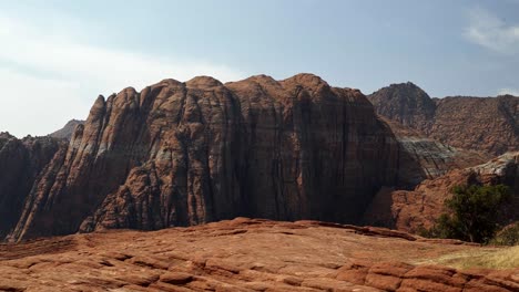 Beautiful-landscape-nature-tilting-up-shot-of-stunning-red-rock-formations-with-dried-petrified-sand-dunes-below-on-a-hike-in-Snow-Canyon-State-Park,-Utah-on-a-warm-sunny-summer-day