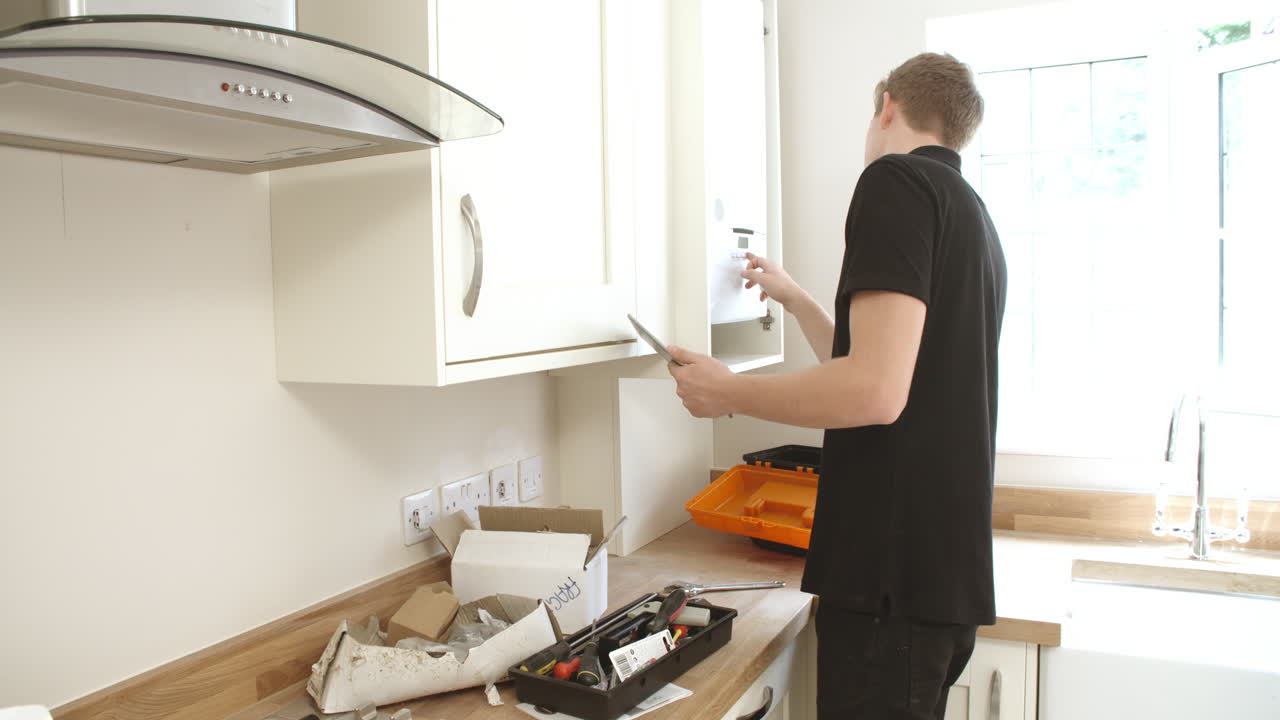 Young technician servicing boiler, using tablet computer