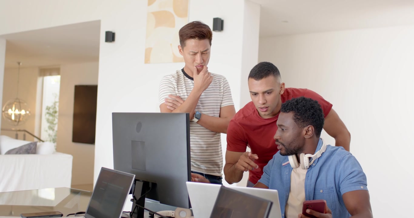 Diverse coworkers leaning over laptop screen, seated man showing red phone, discussing fix at home