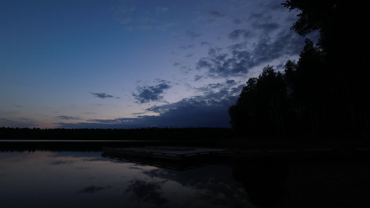 Timelapse di un tranquillo molo sul lago mentre la sera blu della foresta si trasforma in notte