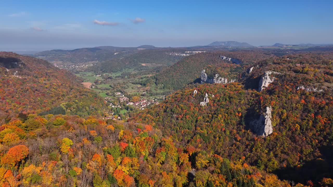 Aerial view of Cirque du Fer à Cheval in France featuring expansive autumn forests, dramatic limestone cliffs and a peaceful valley with scattered houses surrounded by vivid colors under a clear sky