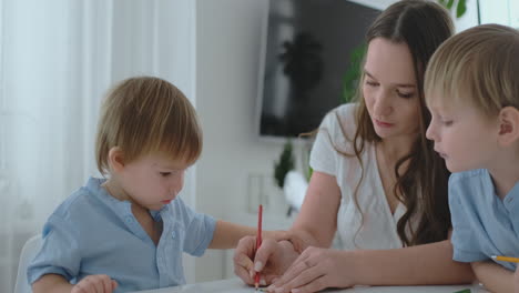 Mom-helps-two-sons-of-2-and-4-years-old-to-do-preschool-homework-to-draw-a-picture-with-pencils