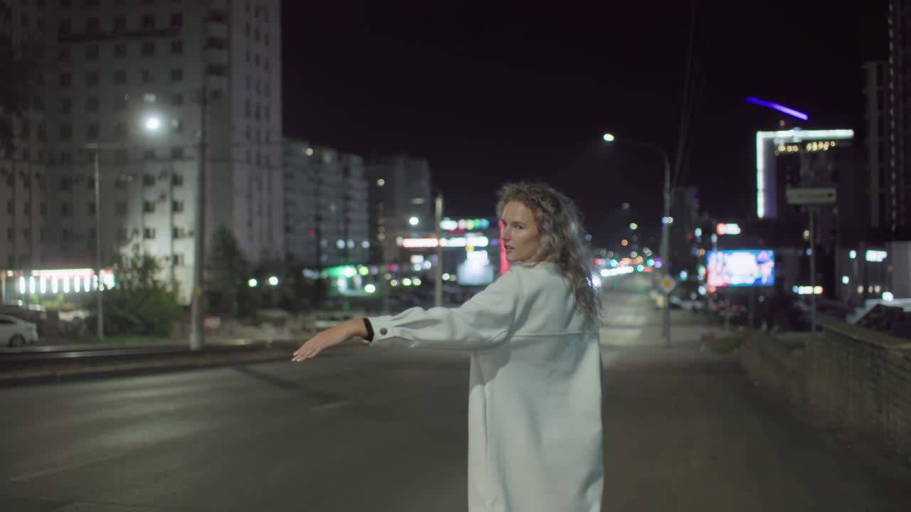 Lady in white coat smiles while trying to stop taxi on city street at night as white car drives past without stopping, surrounded by blurred lights and urban buildings in nighttime environment