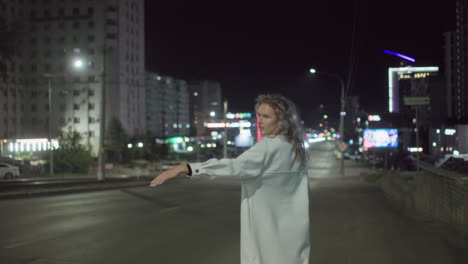 lady in white coat smiles while trying to stop taxi on city street at night as white car drives past without stopping, surrounded by blurred lights and urban buildings in nighttime environment