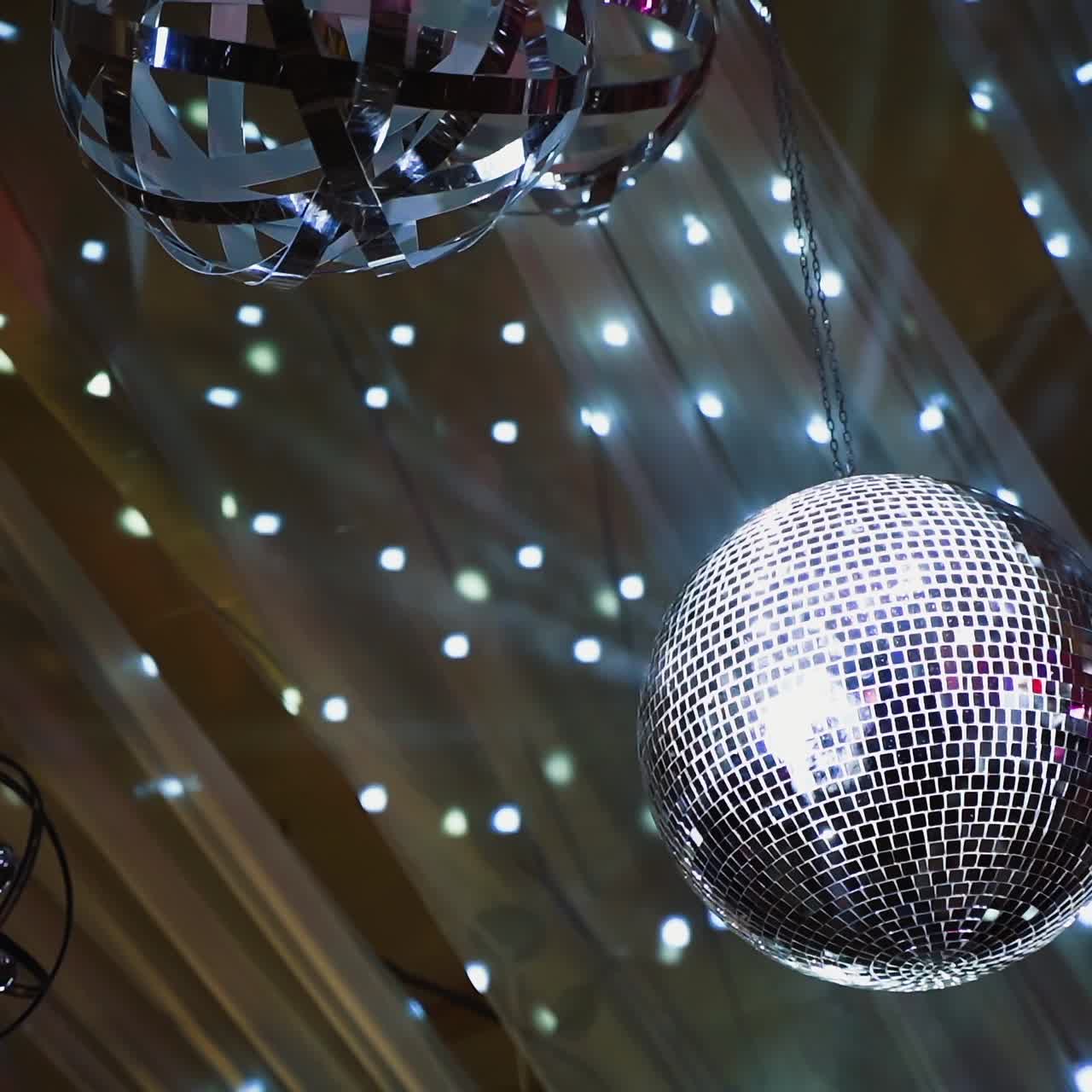 Teto de boate com globo espelhado e luzes. Bola de discoteca prateada girando contra um belo fundo brilhante